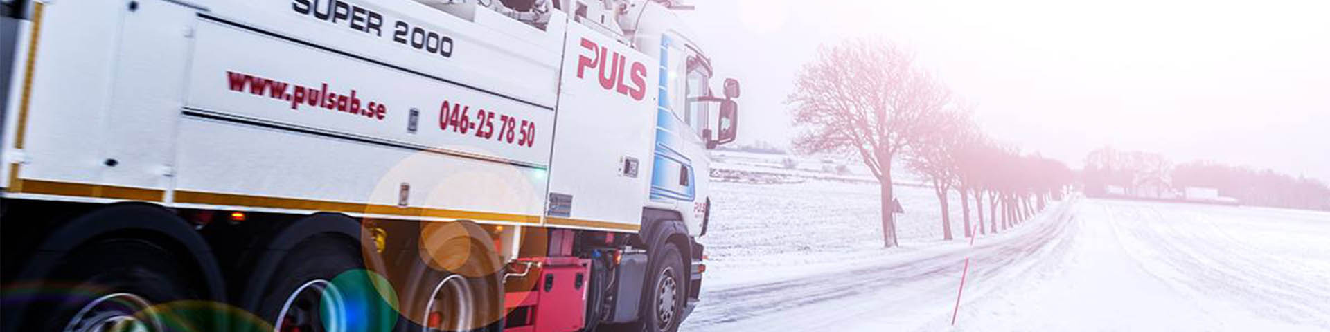 Puls AB lastbil kör på en snöig väg med träd på sidan