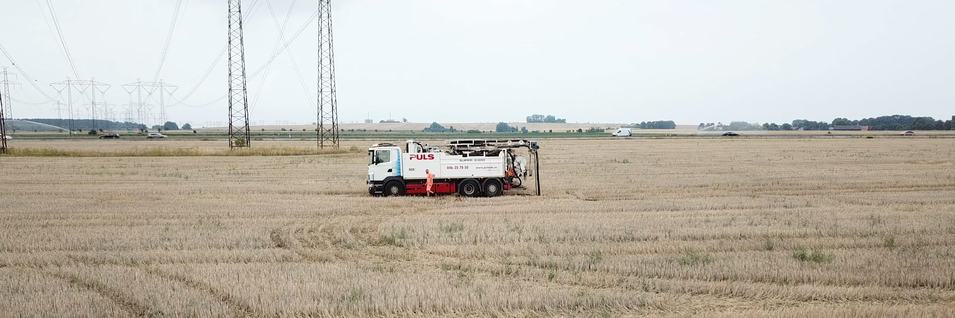 Puls AB lastbil står på en åker med kraftledningar i bakgrunden